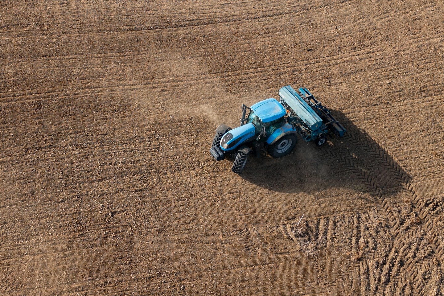 A blue tractor tills a large brown agricultural field.