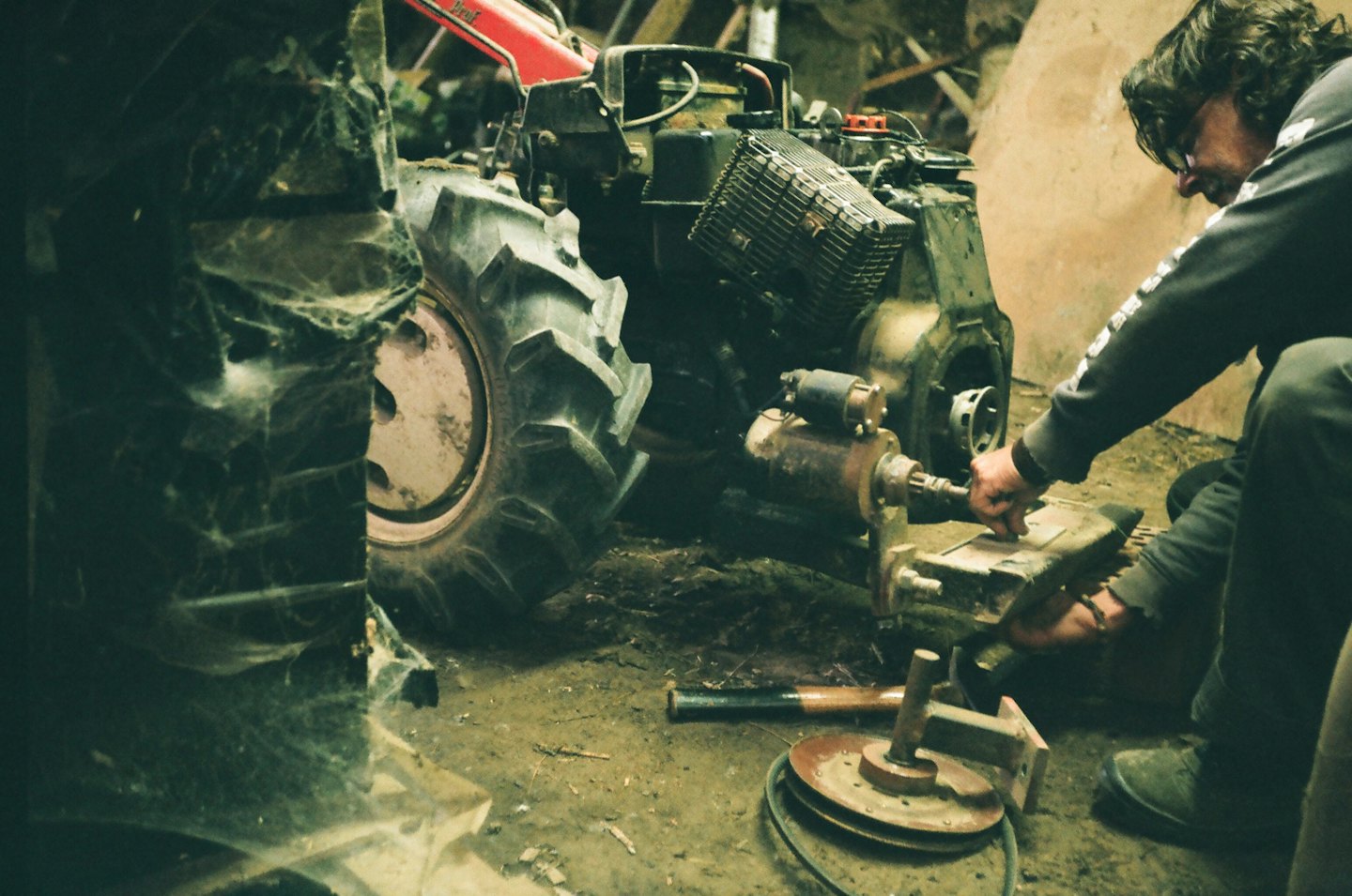 Man repairs engine of red walk-behind tractor in workshop.
