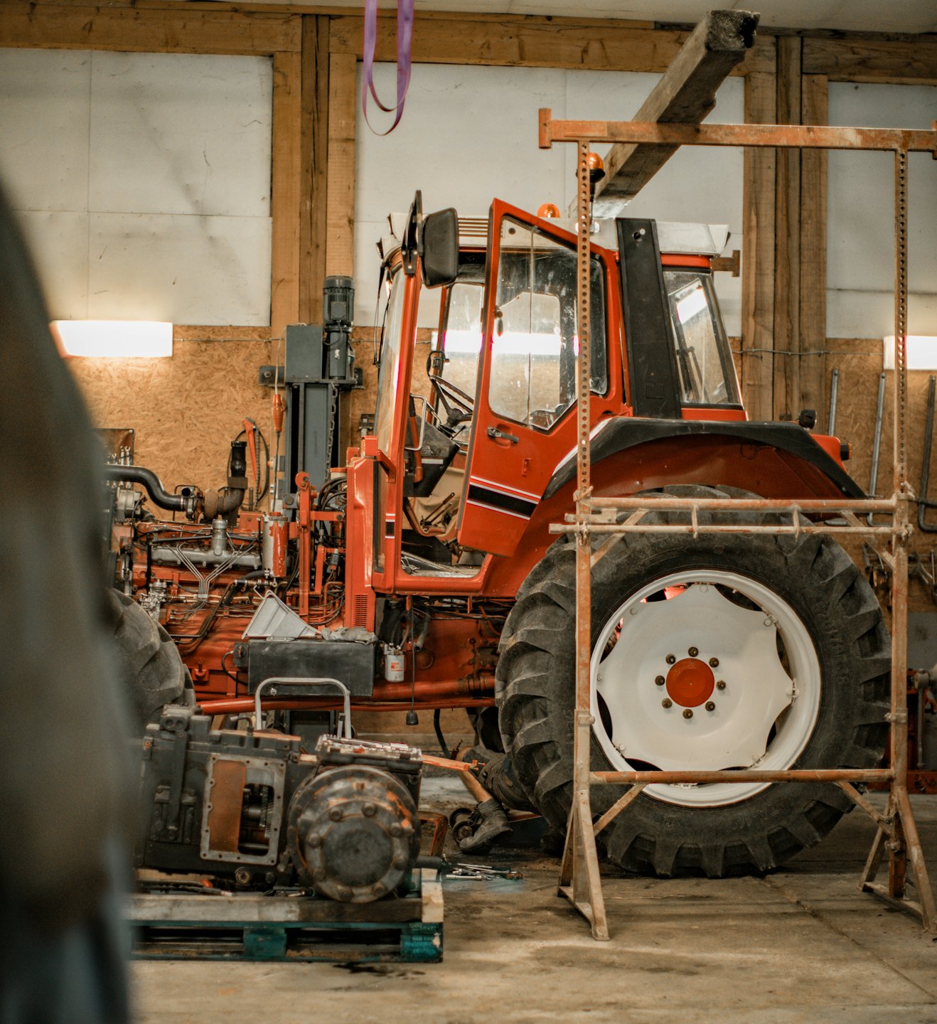 A red tractor with its engine exposed sits in a workshop.