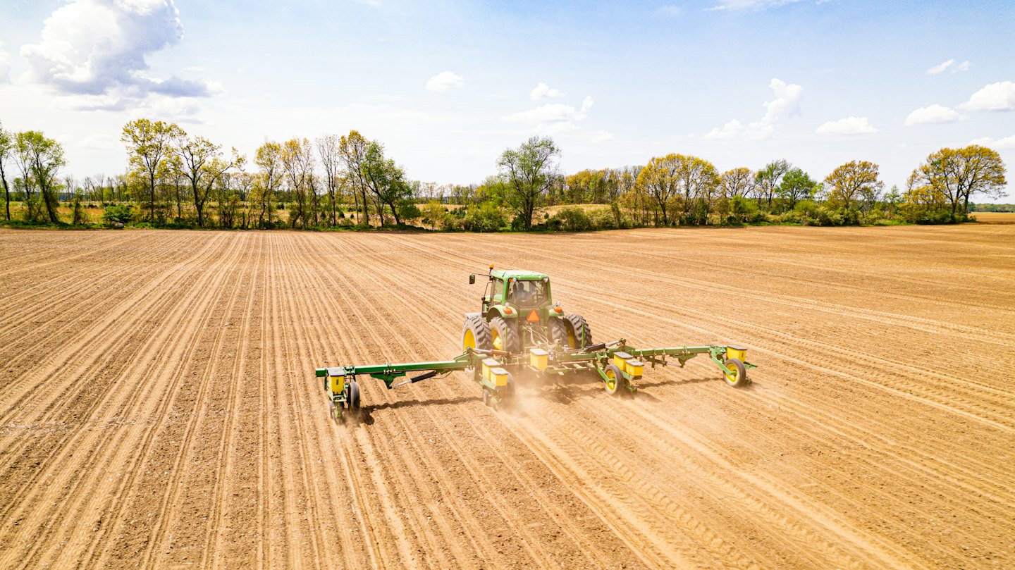 A green tractor tills a large agricultural field.