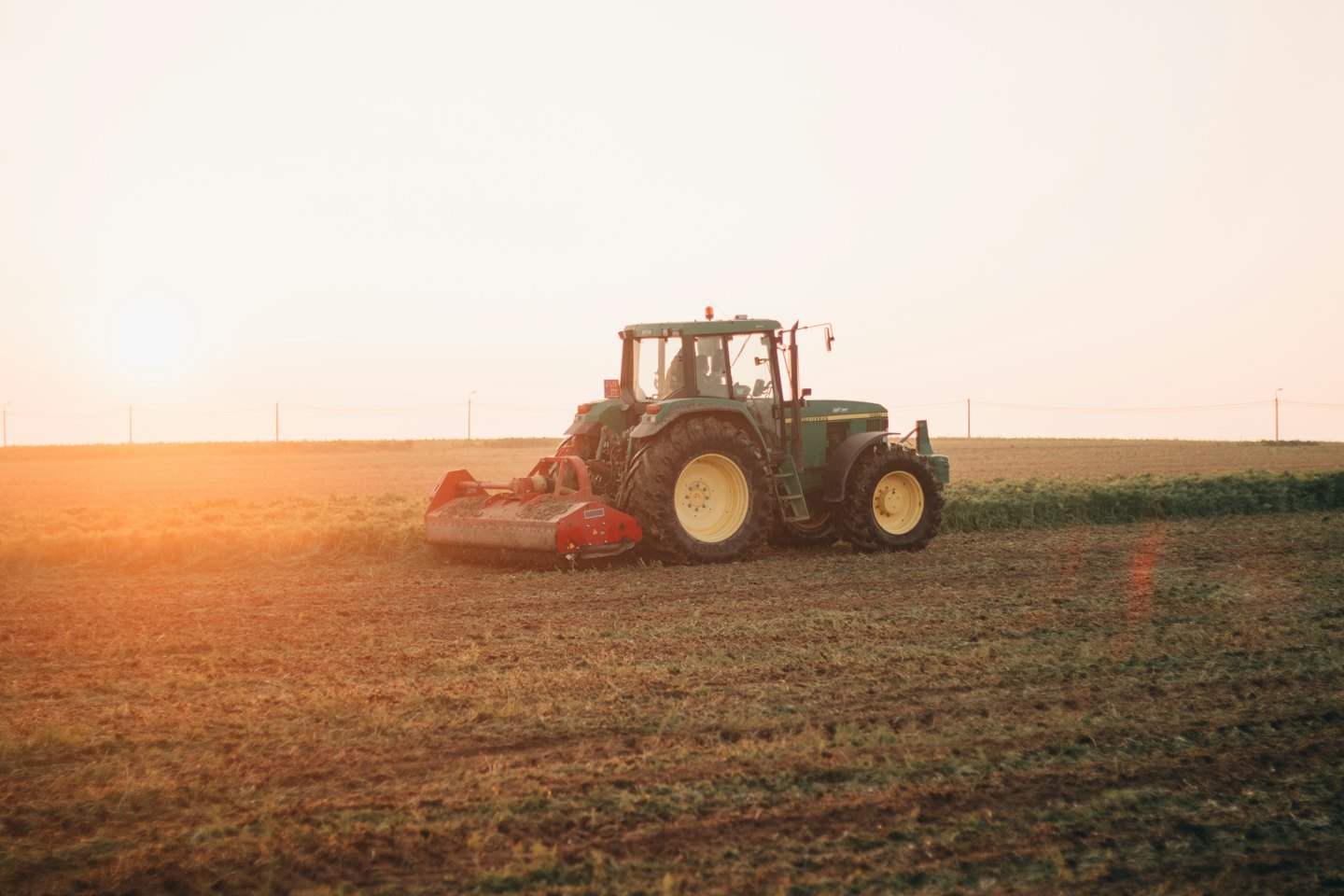 A green John Deere tractor tills a field at sunrise.